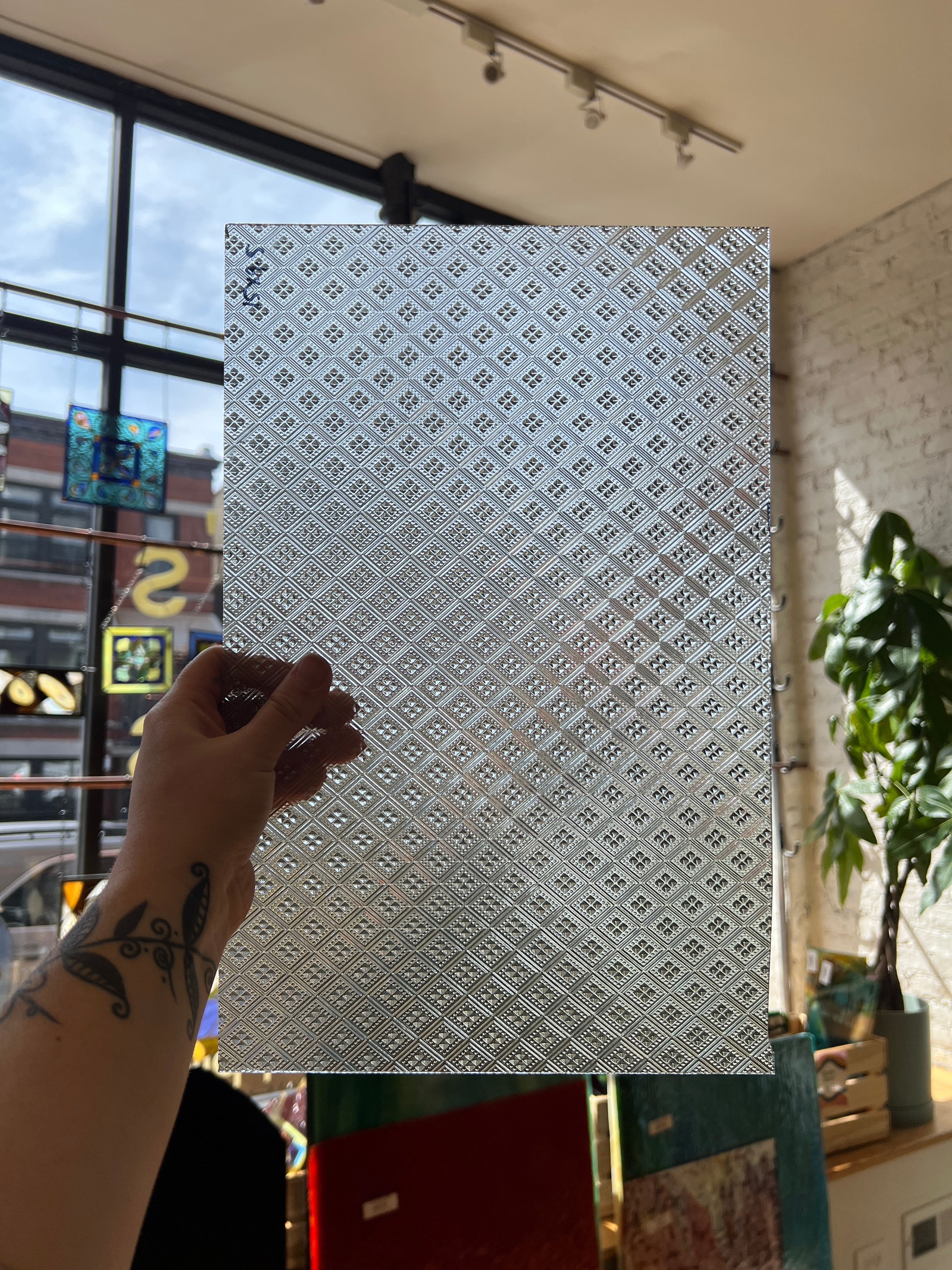 Hand holding a patterned sheet of glass against a blurred indoor background