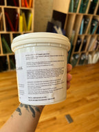 White container of glass putty with text held by a person, blurred background