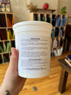 Hand holding a white container of glass putty with instructional text on a blurred indoor background