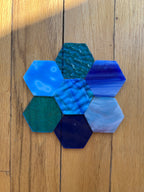Hexagonal glass pieces in various blue and green colors on a wooden surface