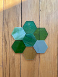 Hexagonal glass pieces in greens on a wooden surface
