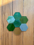 Hexagonal glass pieces in greens on a wooden surface