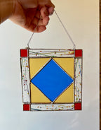 Stained glass panel with blue diamond and red borders held by a hand against a white background