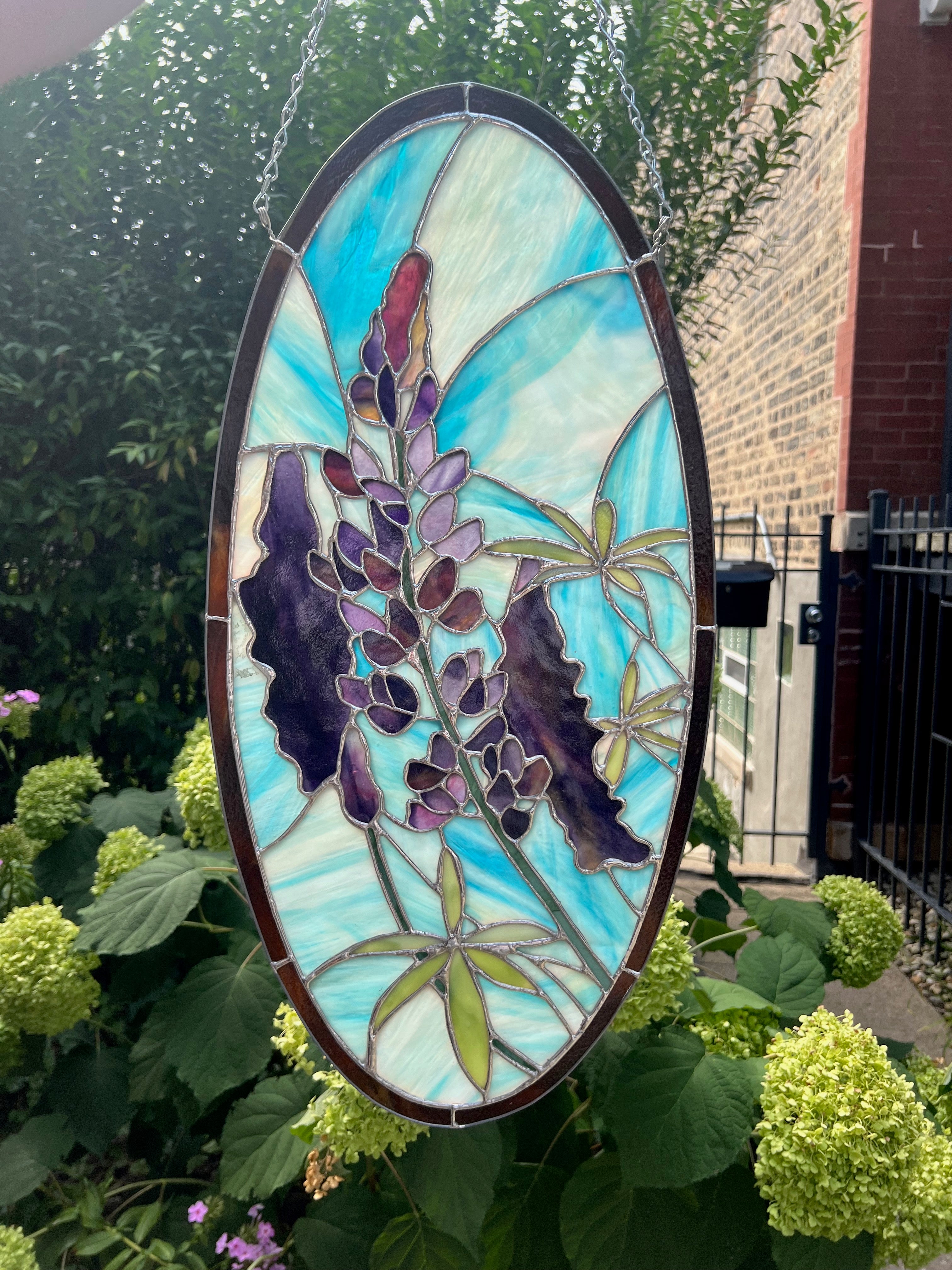 Stained glass panel with floral design hanging among green plants