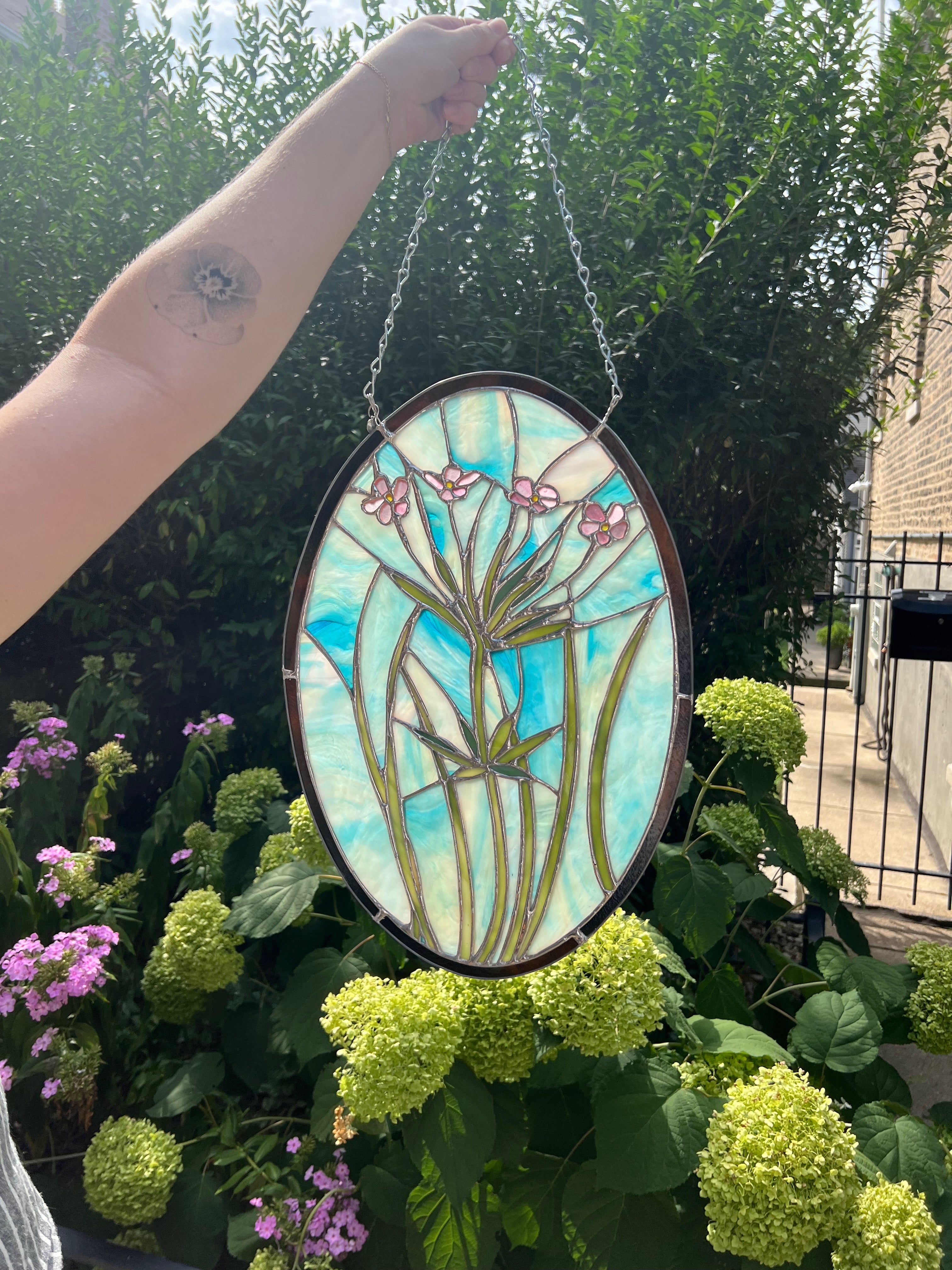 Stained glass panel with floral design held in front of greenery