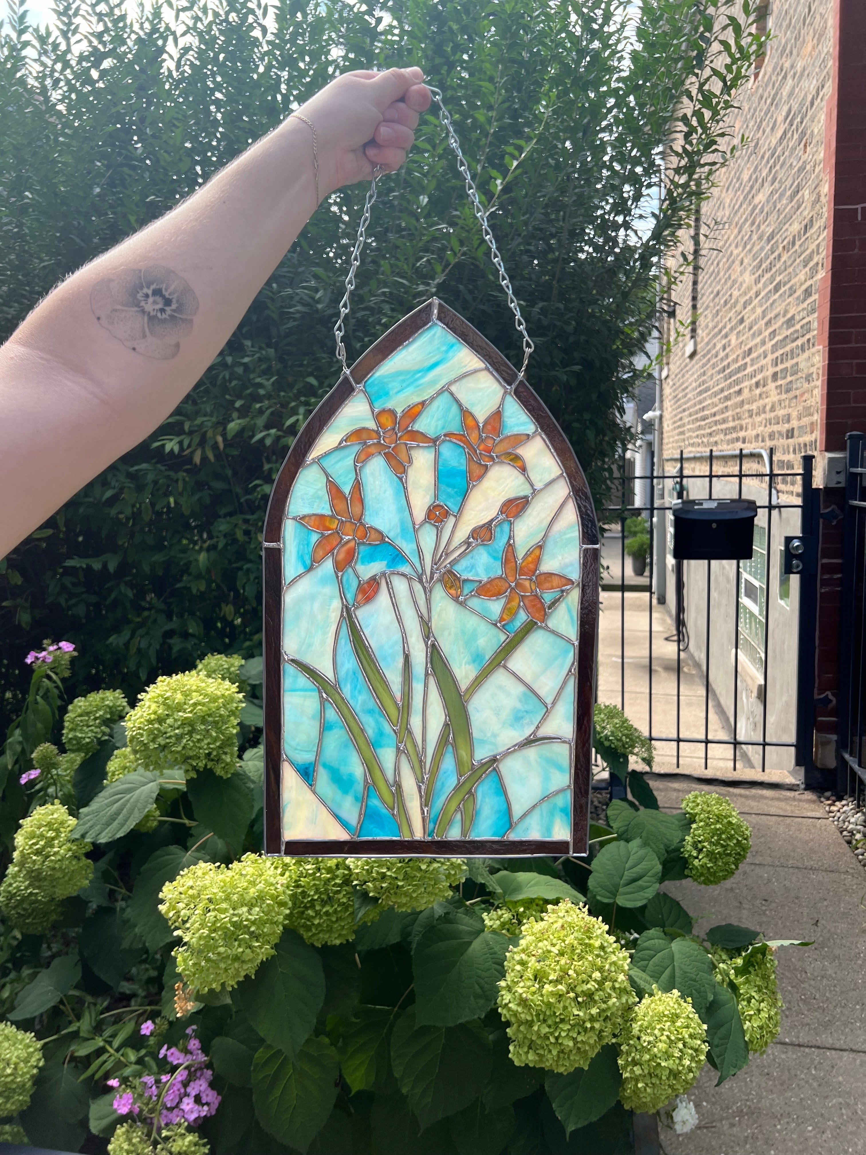 Stained glass panel with floral design held by a person outdoors.