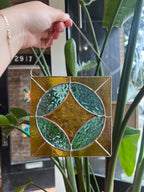 Stained glass panel with leaf design held by a hand in front of a plant