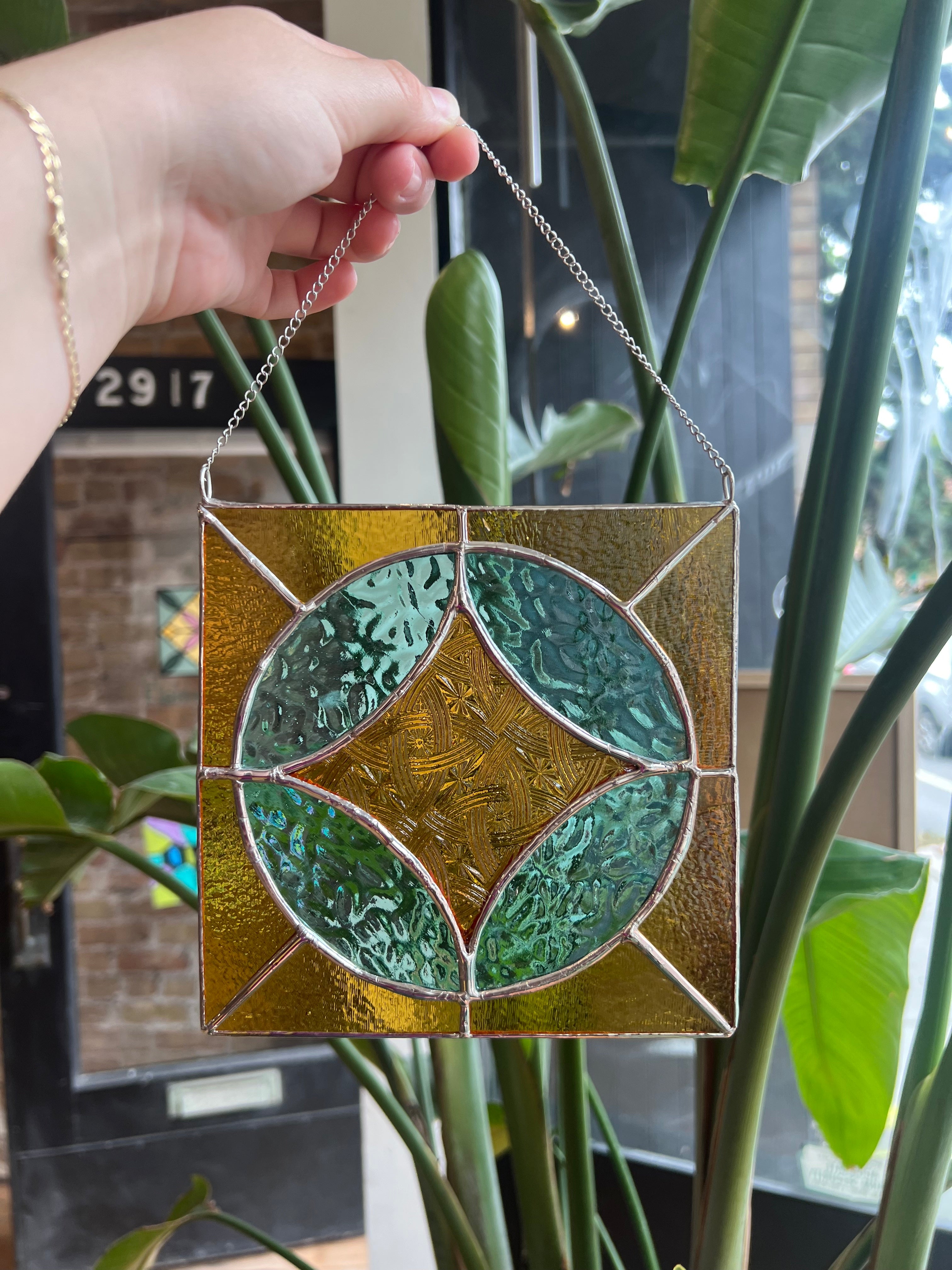 Stained glass panel with leaf design held by a hand in front of a plant
