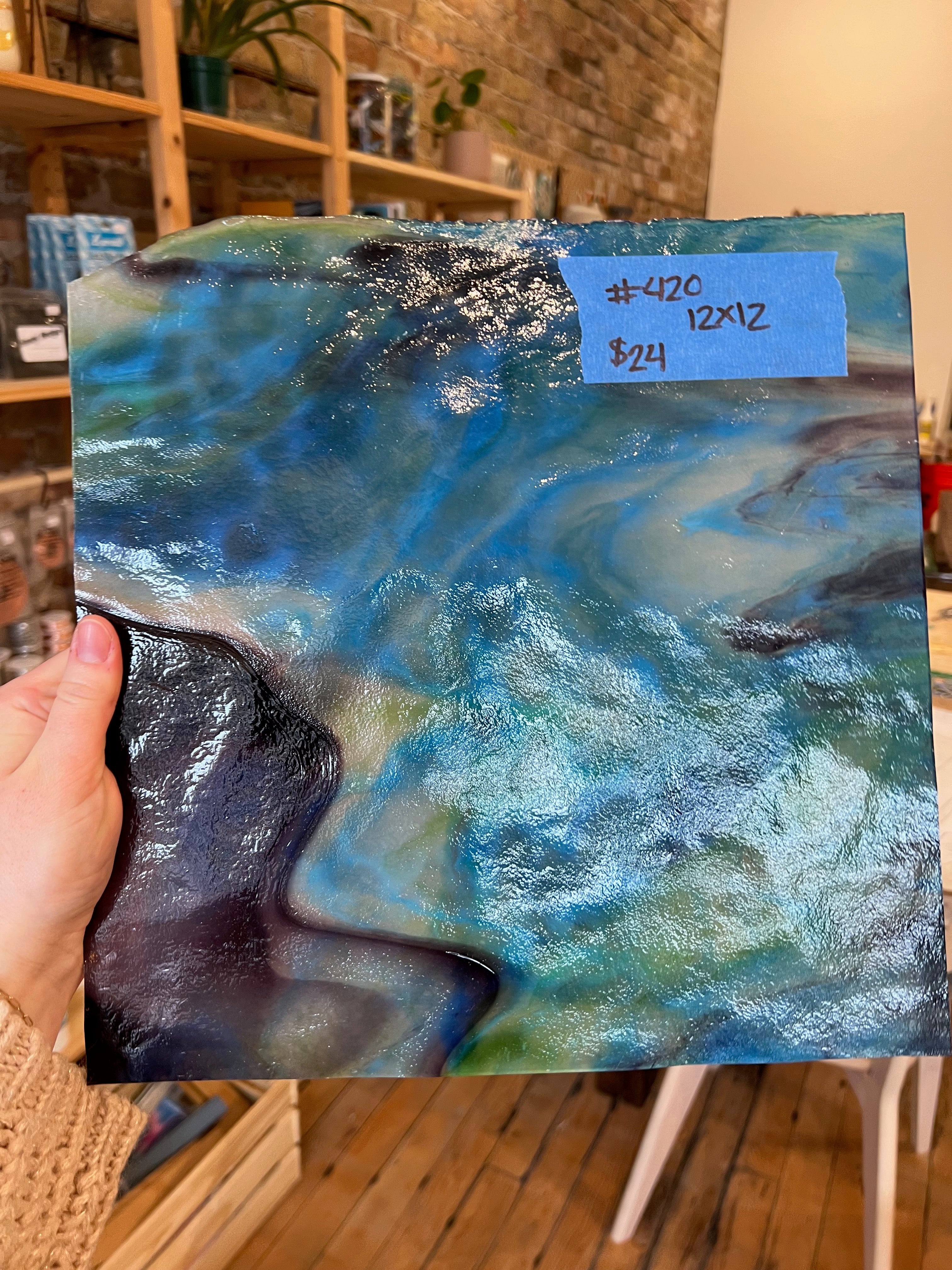 Hand holding a piece of swirled blue glass with a blue label indicating size and price.