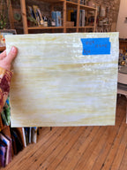 Person holding a large sheet of glass with a textured surface in a room with wooden floors and shelves.