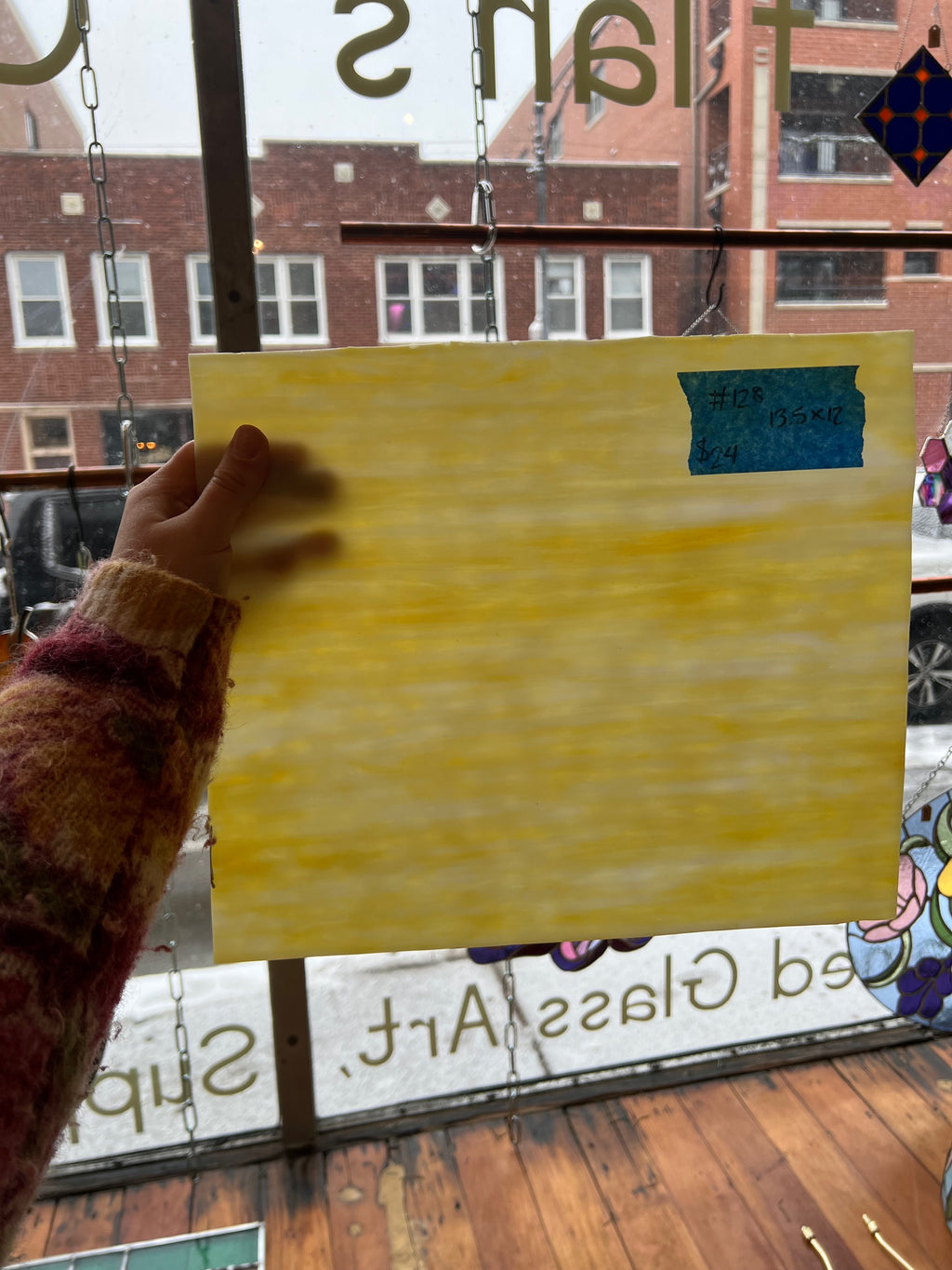 Person holding a yellow piece of glass in front of a store window with a blurred street view.