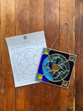 Stained glass panel with a chain on a wooden surface next to a pattern sheet.