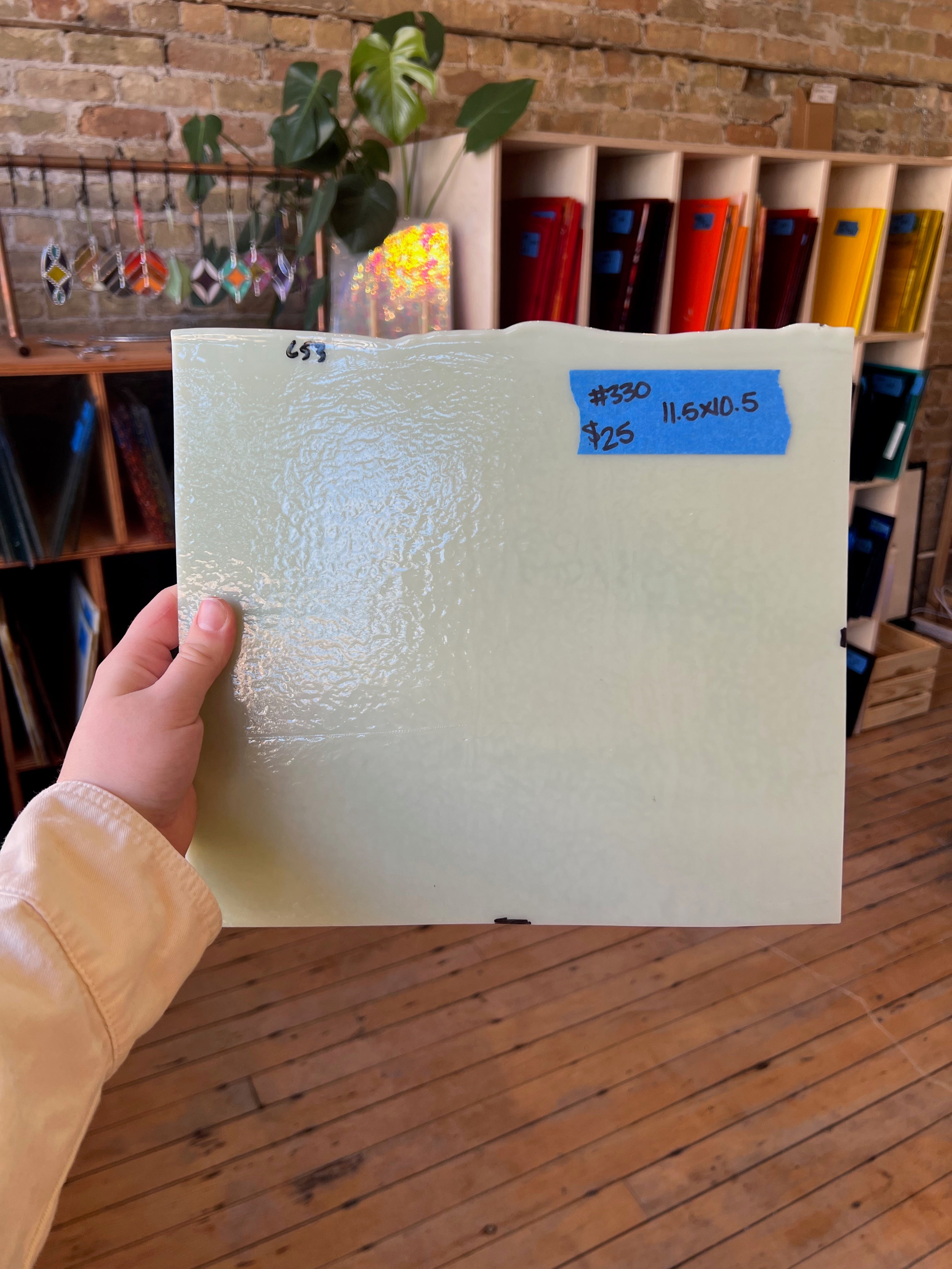 Hand holding a textured white piece of stained glass with a blue label in an art supply store.