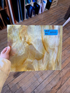 Person holding a large piece of glass with a label on a wooden floor.