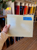 Hand holding a sheet of glass with a blue label in front of a bookshelf.