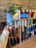 Person holding a clear glass sheet with a brick wall and shelves in the background