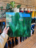 Person holding a green swirled piece of glass in front of a brick wall and bookshelf.