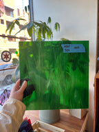Person holding a green piece of glass with plant imagery in an indoor setting