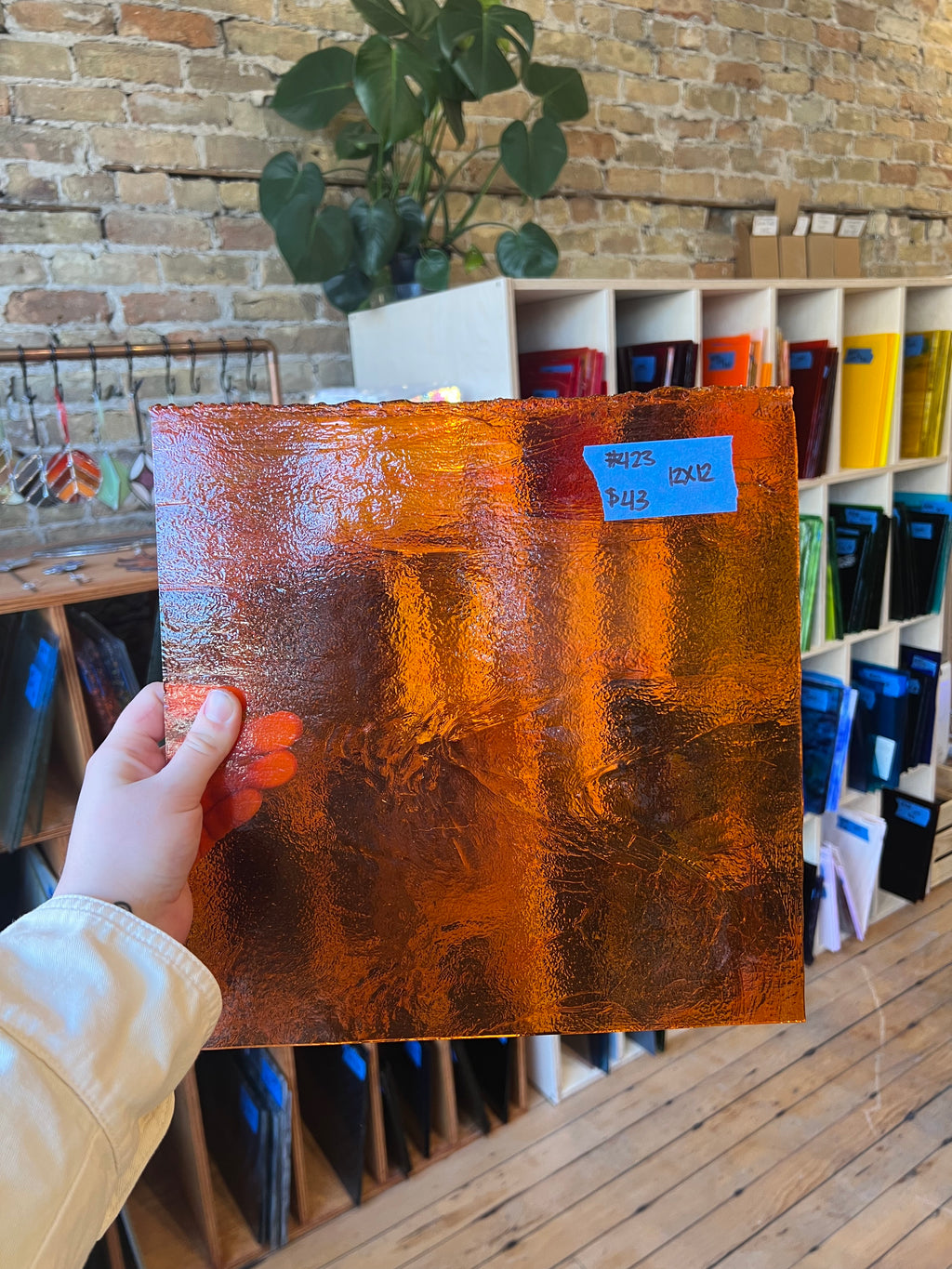 Person holding a textured brown piece of glass with a brick wall and shelves in the background
