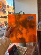 Hand holding a textured orange piece of glass with a blurred indoor background