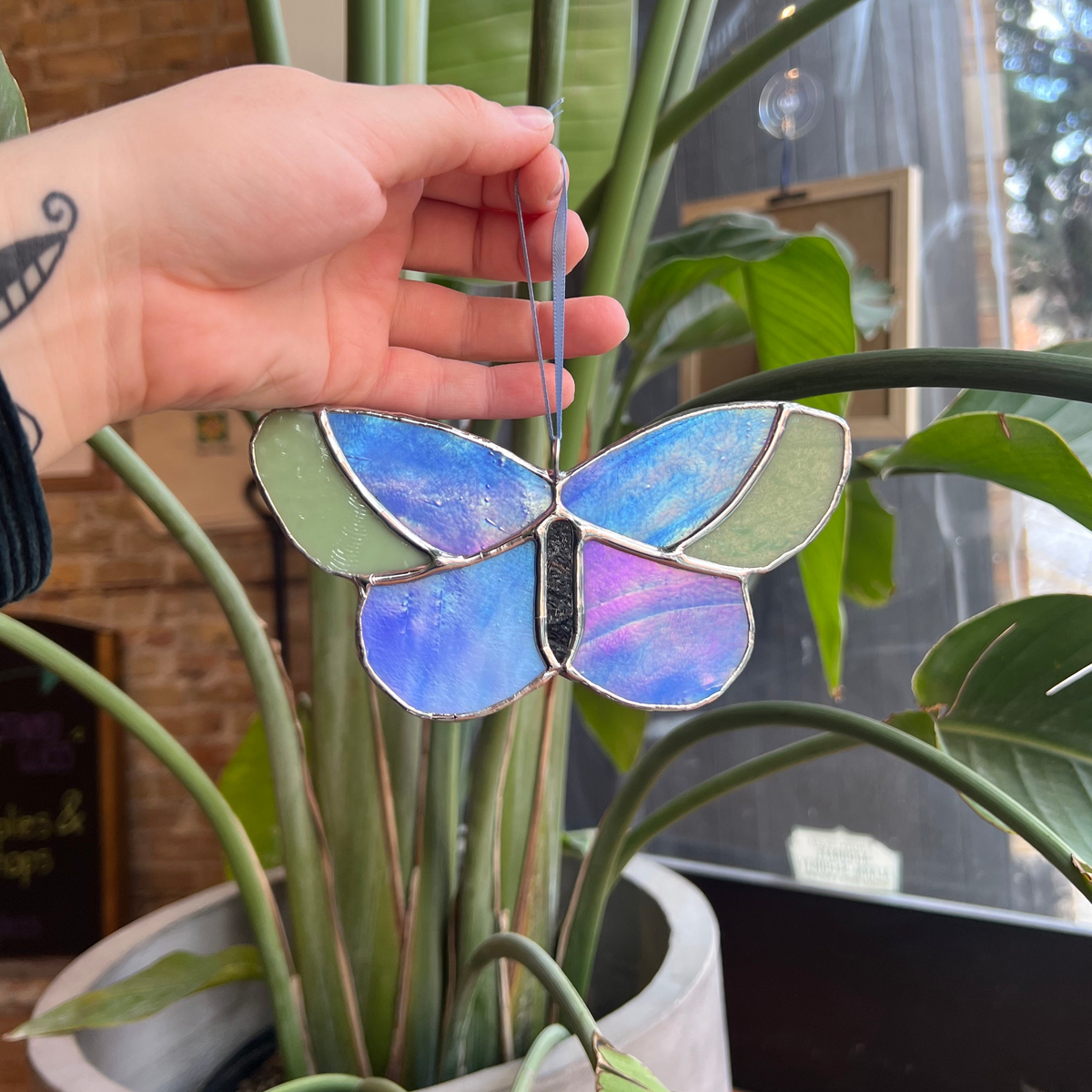 Stained glass butterfly held by a hand in front of a plant