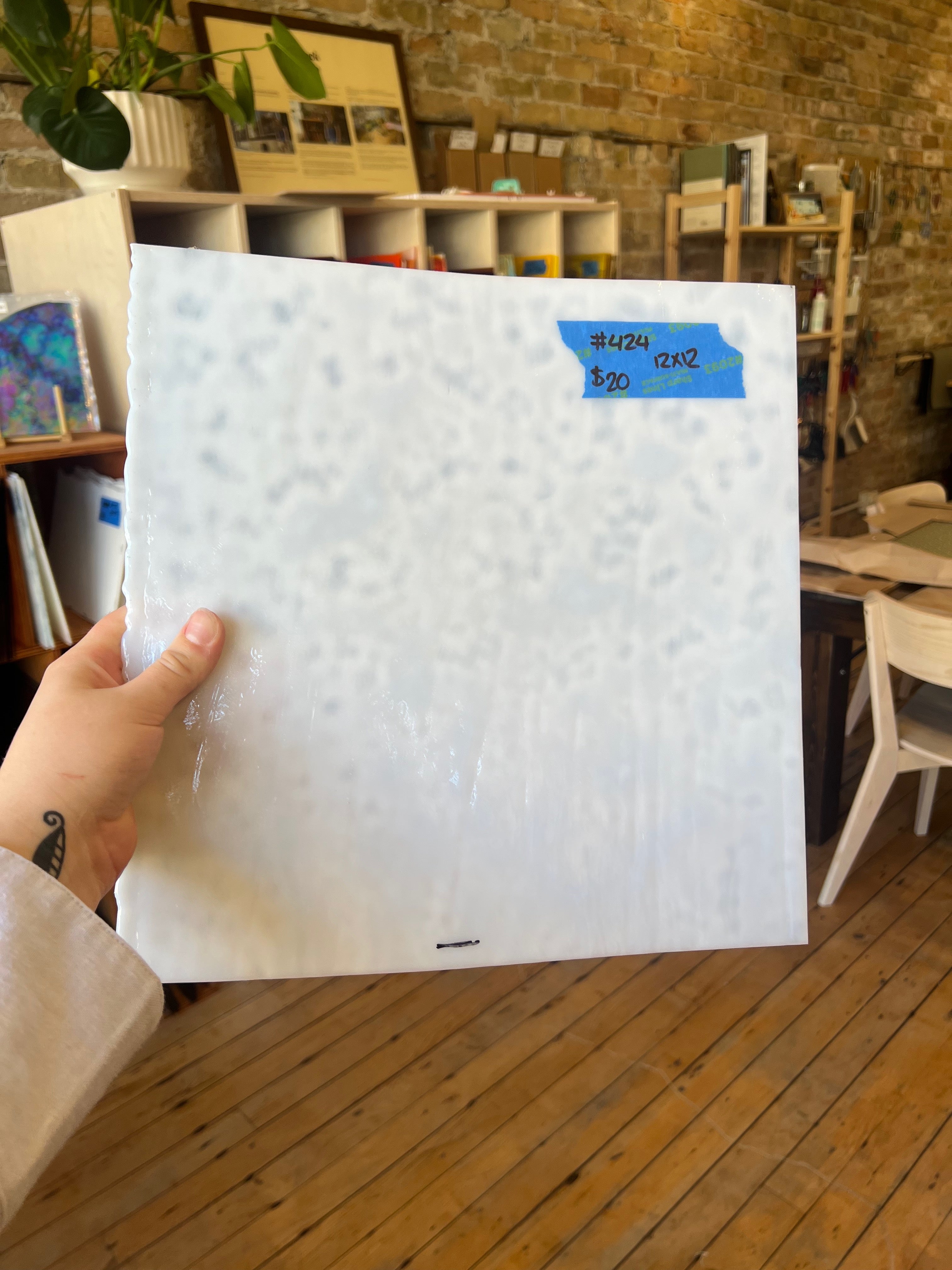 Person holding a large white piece of mottled stained glass in an indoor setting with furniture and decor.