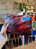 Person holding a piece of red stained glass with a brick wall and bookshelf in the background