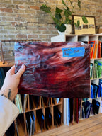 Person holding a piece of red stained glass with a brick wall and bookshelf in the background