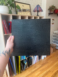 Person holding a black textured piece of glass in a room with shelves and decor