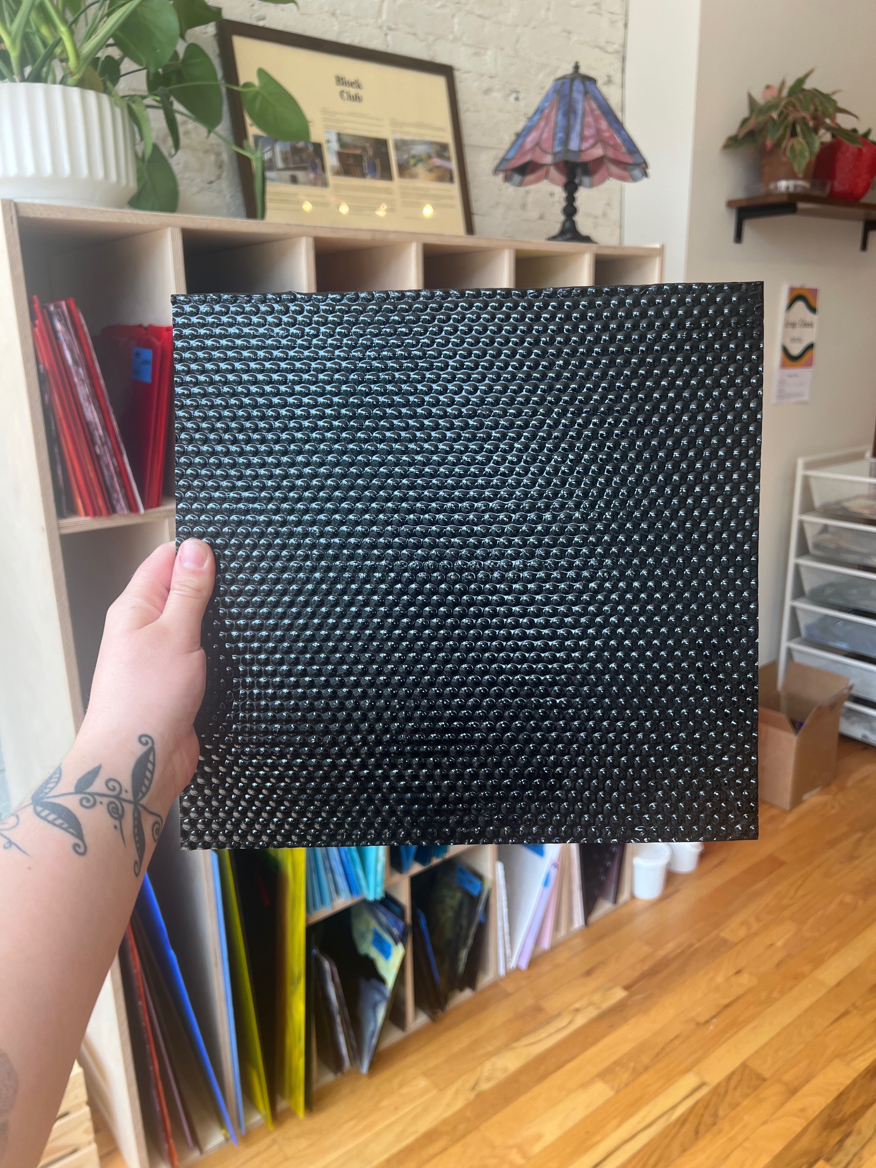 Person holding a black textured piece of glass in a room with shelves and decor
