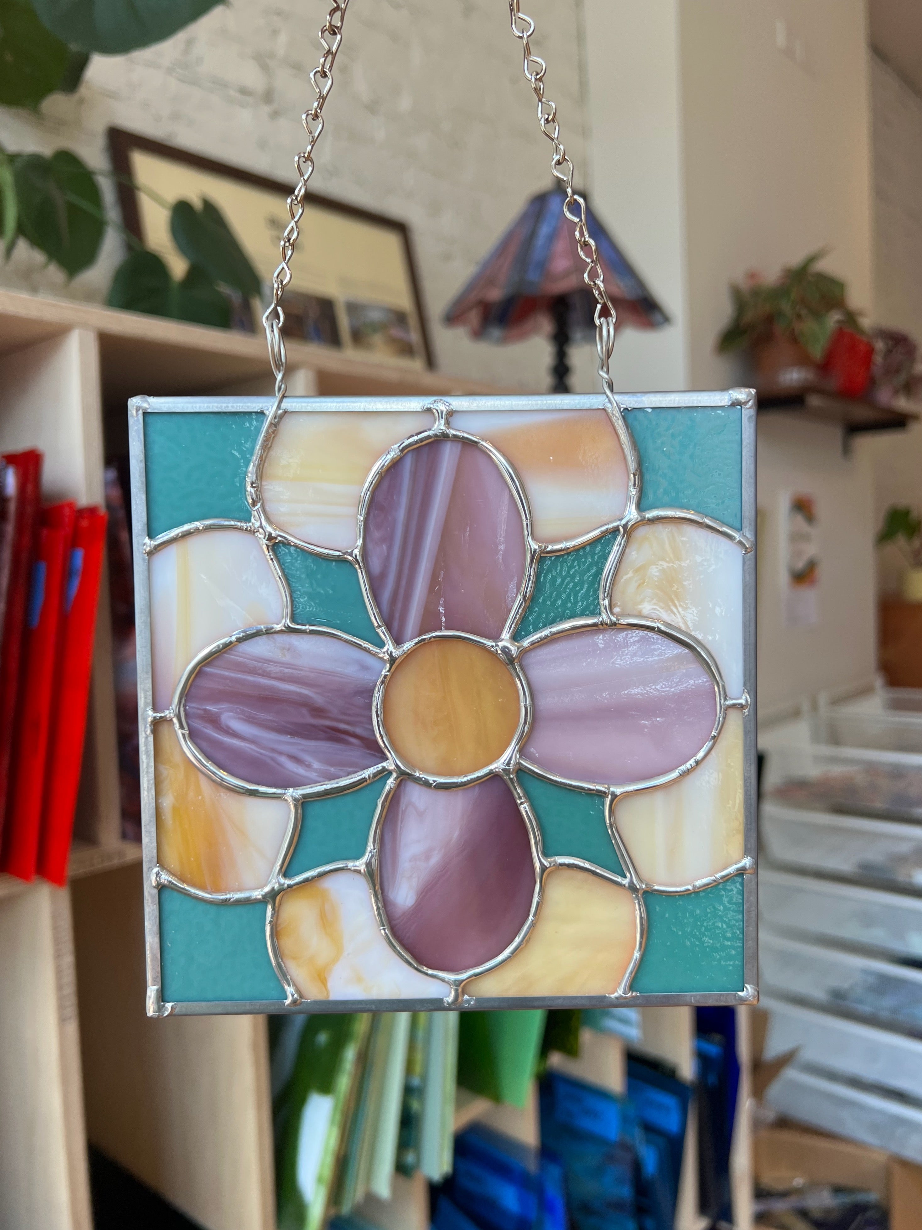 Stained glass flower panel hanging in a room with books and decor.