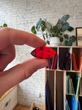 Hand holding a red gem with a bookshelf and plants in the background