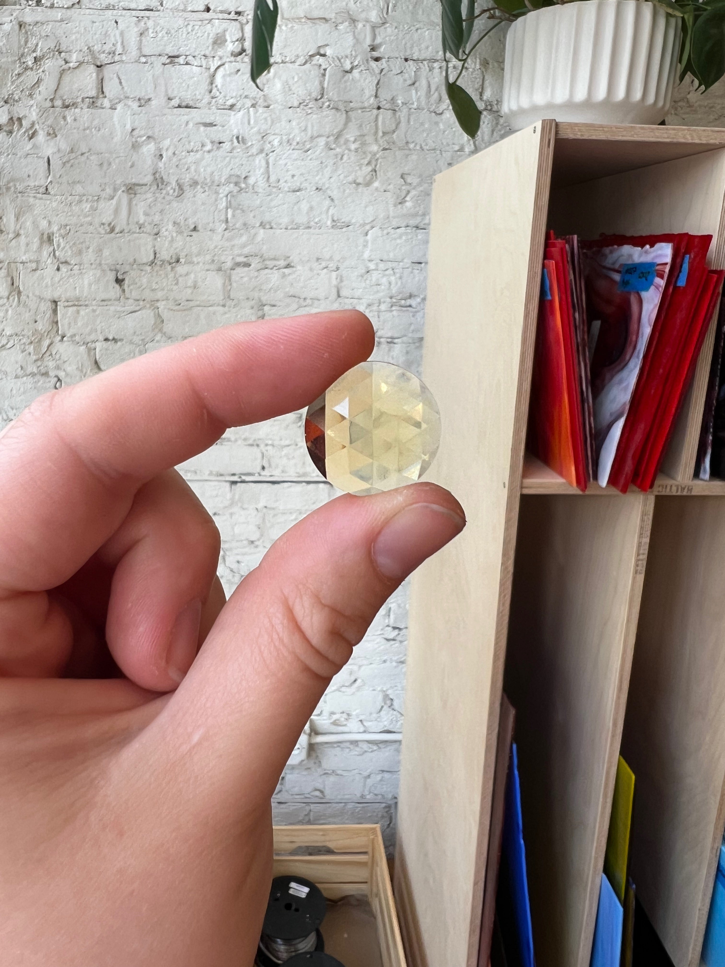 Hand holding a clear crystal in front of a bookshelf with colorful books.