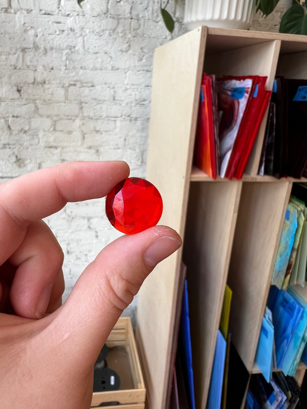 Hand holding a red gemstone in front of a bookshelf with colorful books.