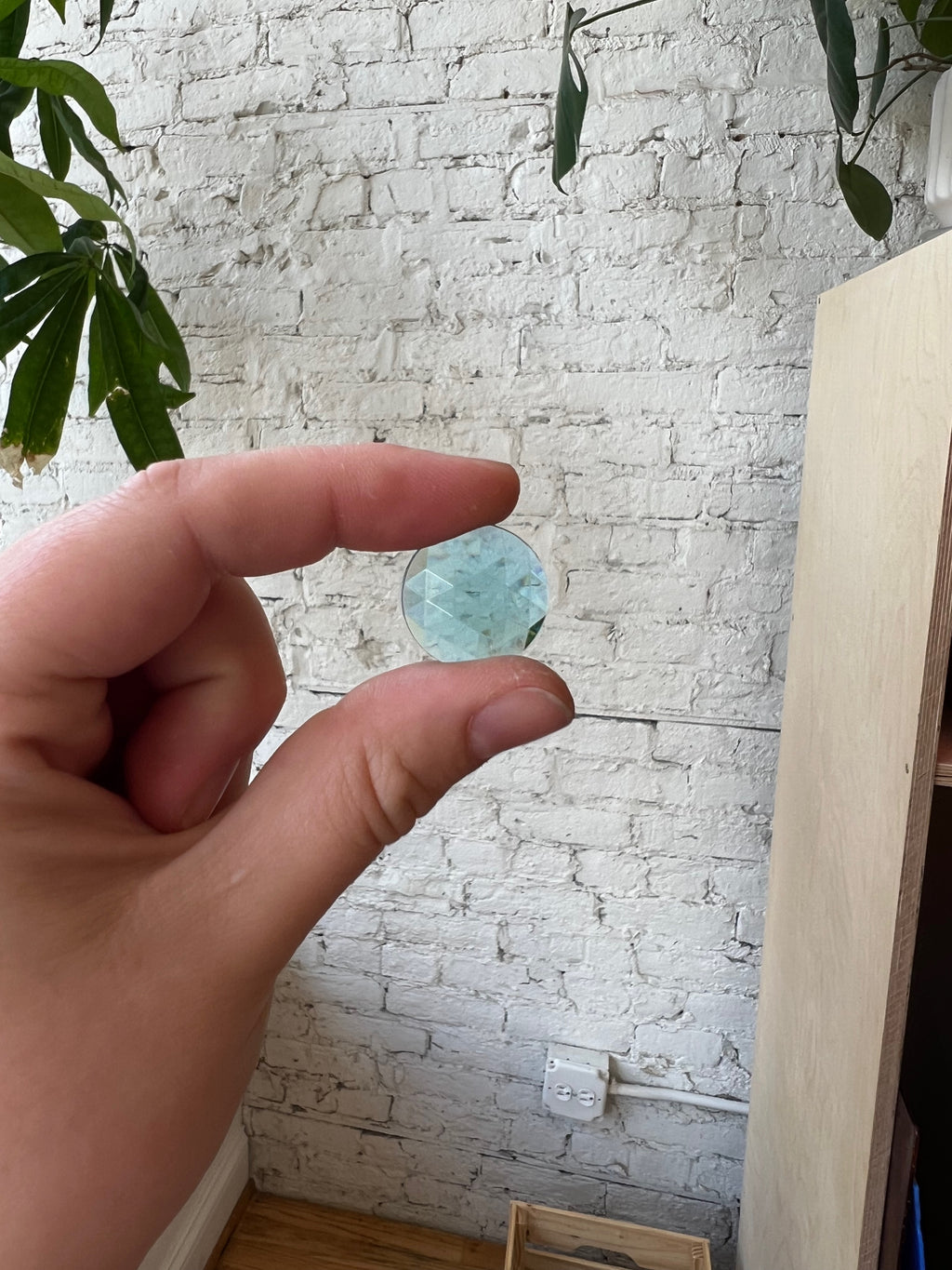 Hand holding a gemstone against a white brick wall.