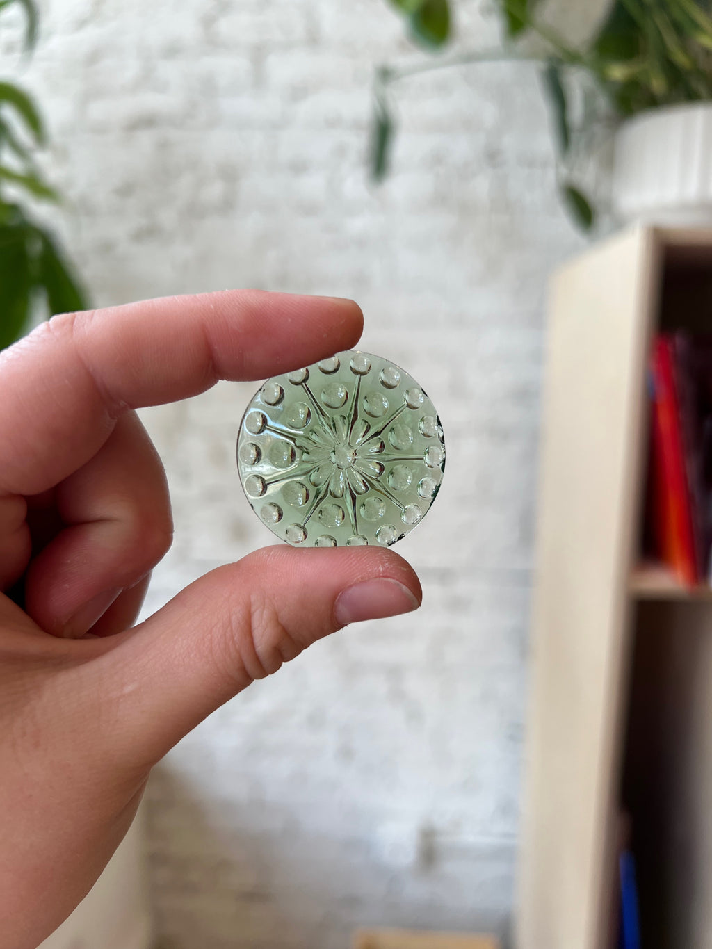 Hand holding a green decorative gem with intricate patterns against a blurred indoor background