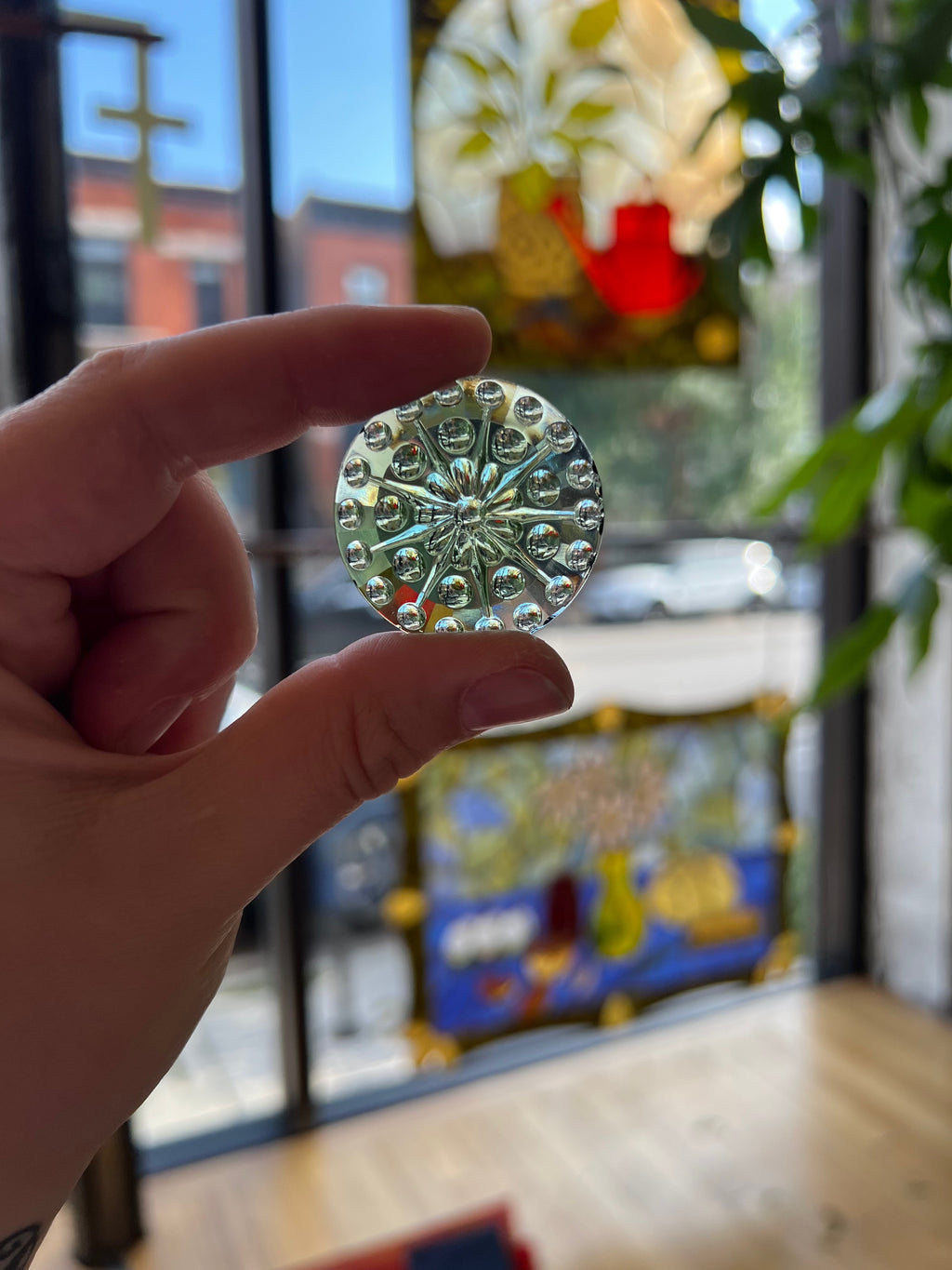 Hand holding a decorative gem with a blurred colorful background