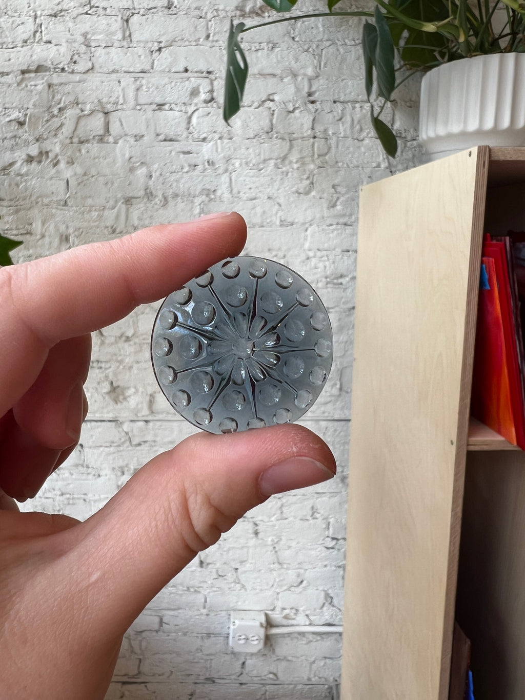 Hand holding a round gem with a textured surface against a light brick wall.
