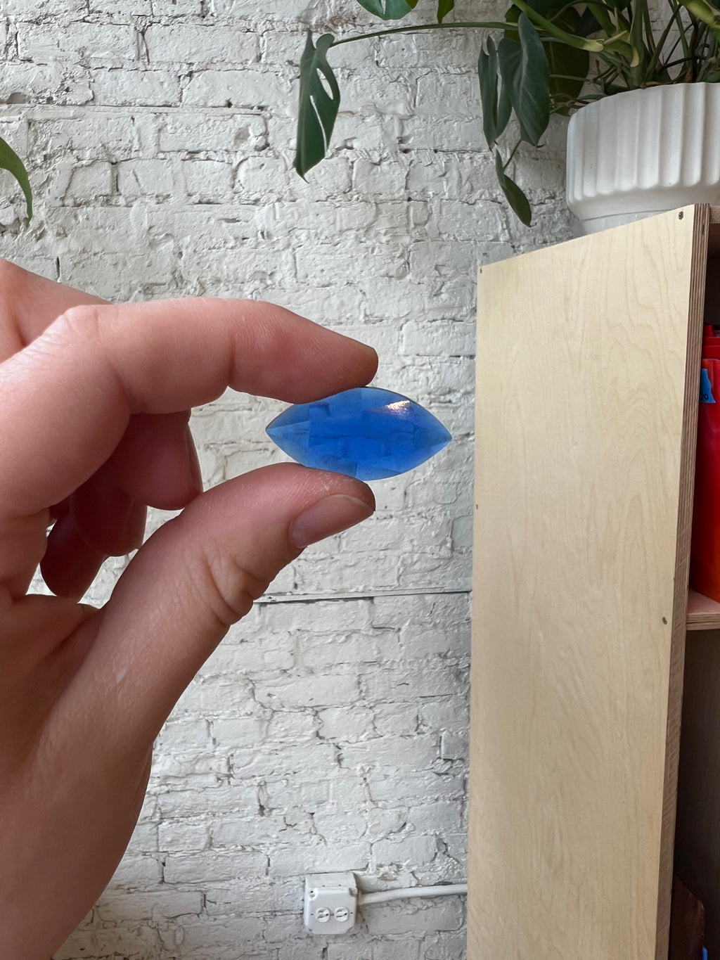 Hand holding a blue gem against a white brick wall background