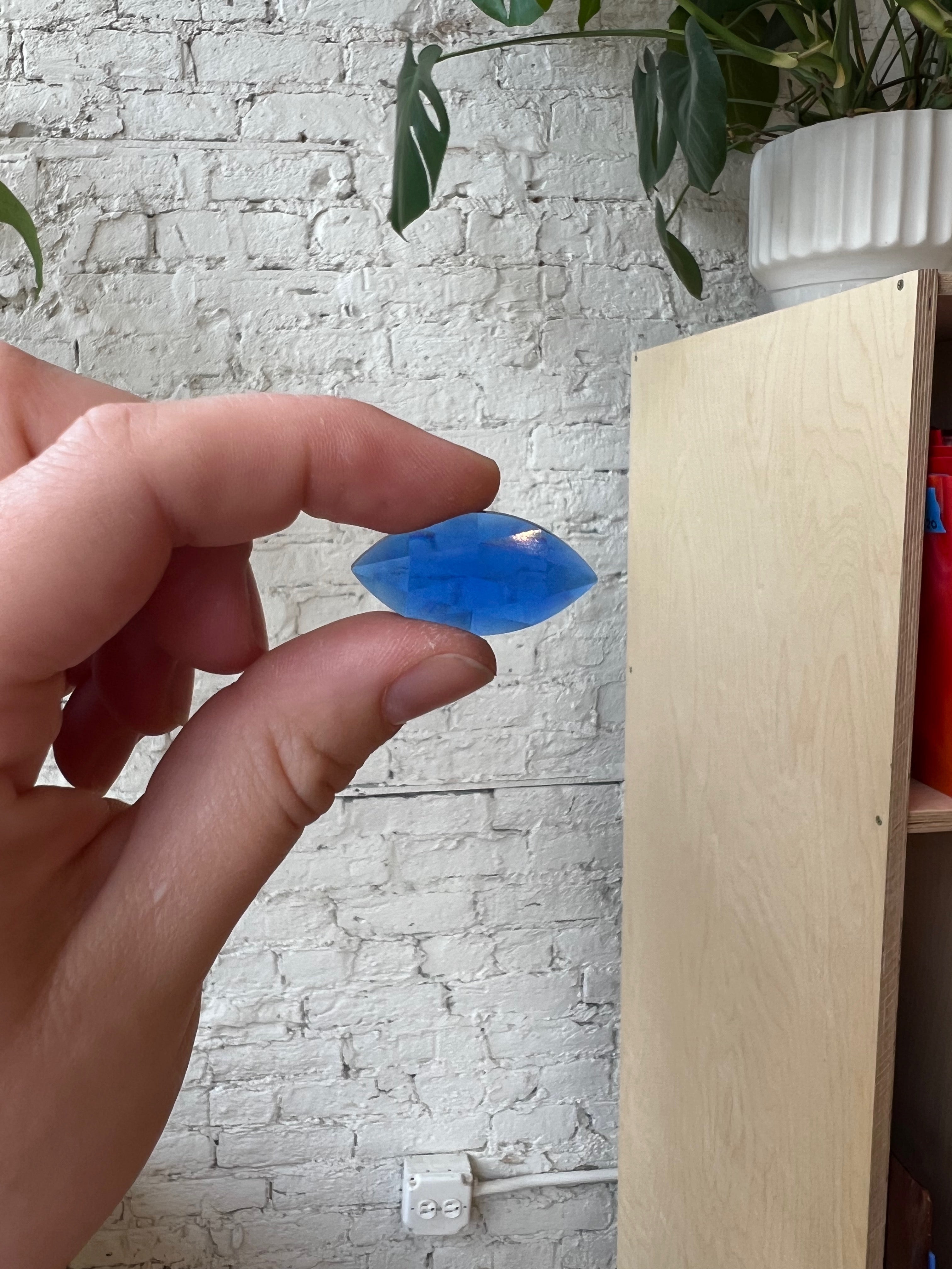 Hand holding a blue gem against a white brick wall background