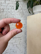 Hand holding a transparent orange gemstone against a light gray brick wall.