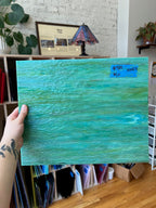 Person holding a green textured piece of glass with a blurred indoor background