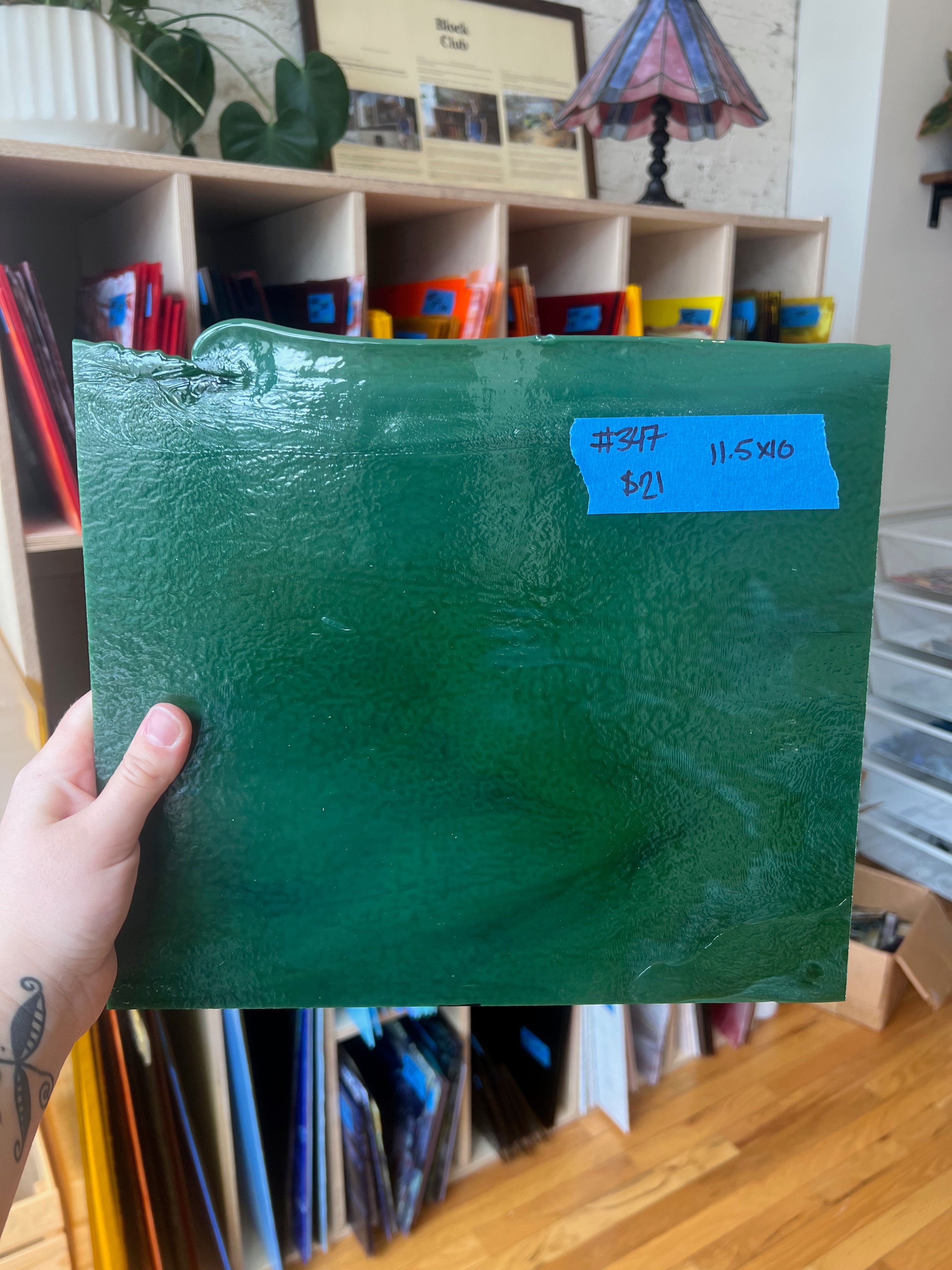 Green piece of glass held by a hand with a price tag attached, in an indoor setting.