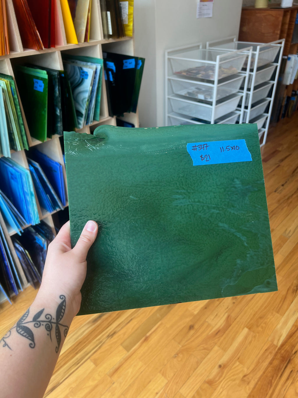 Person holding a green piece of glass with a bookshelf and storage units in the background