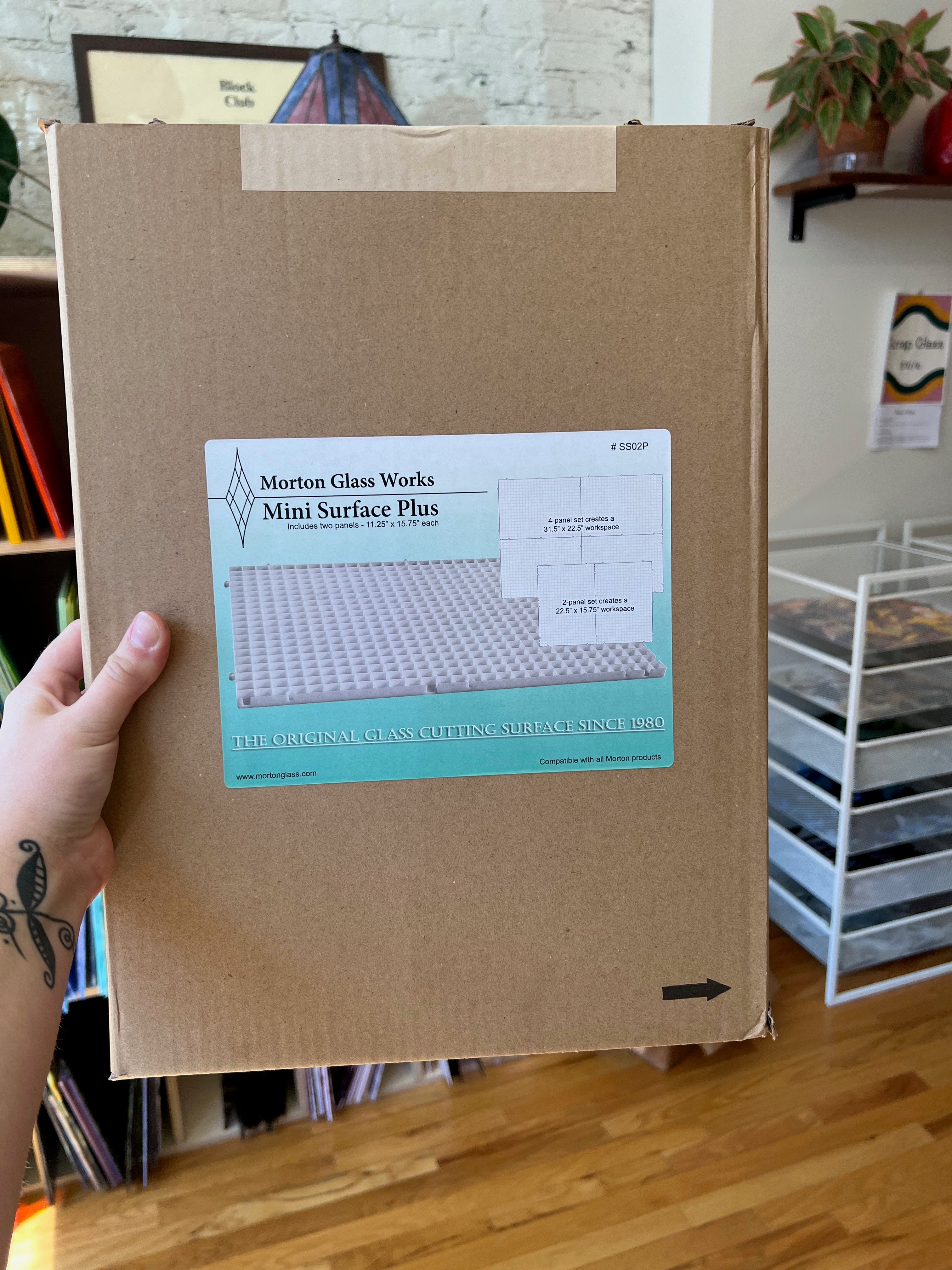 Cardboard box with Morton Glass Works label held by a hand in an indoor setting.