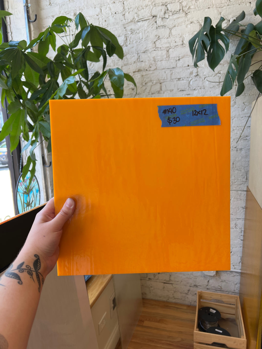 Orange sheet of glass held by a hand with a plant and white brick wall in the background