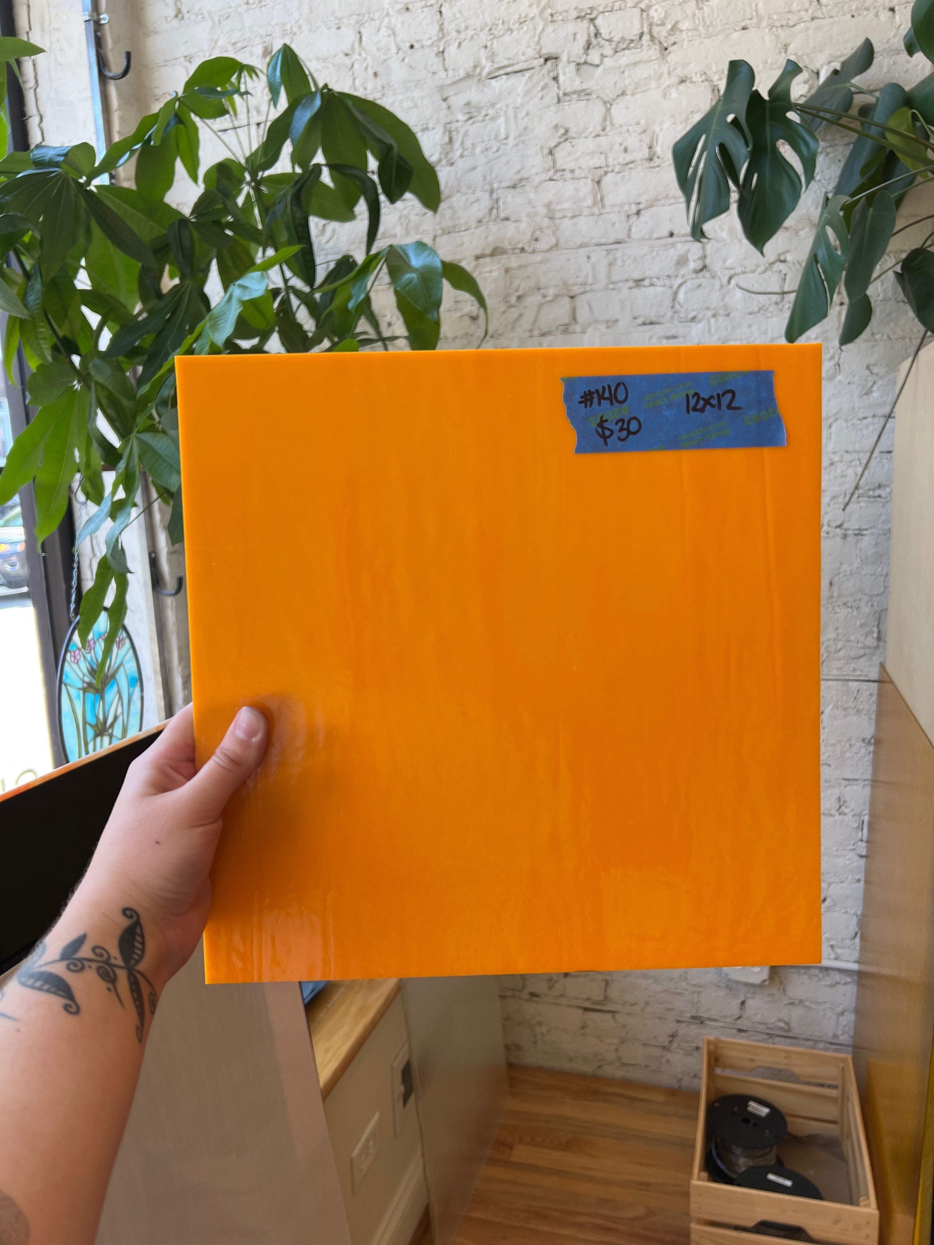 Orange sheet of glass held by a hand with a plant and white brick wall in the background