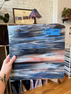 Hand holding a piece of abstract glass with a blue and pink color scheme, labeled '12x12' and '44' in a room setting.