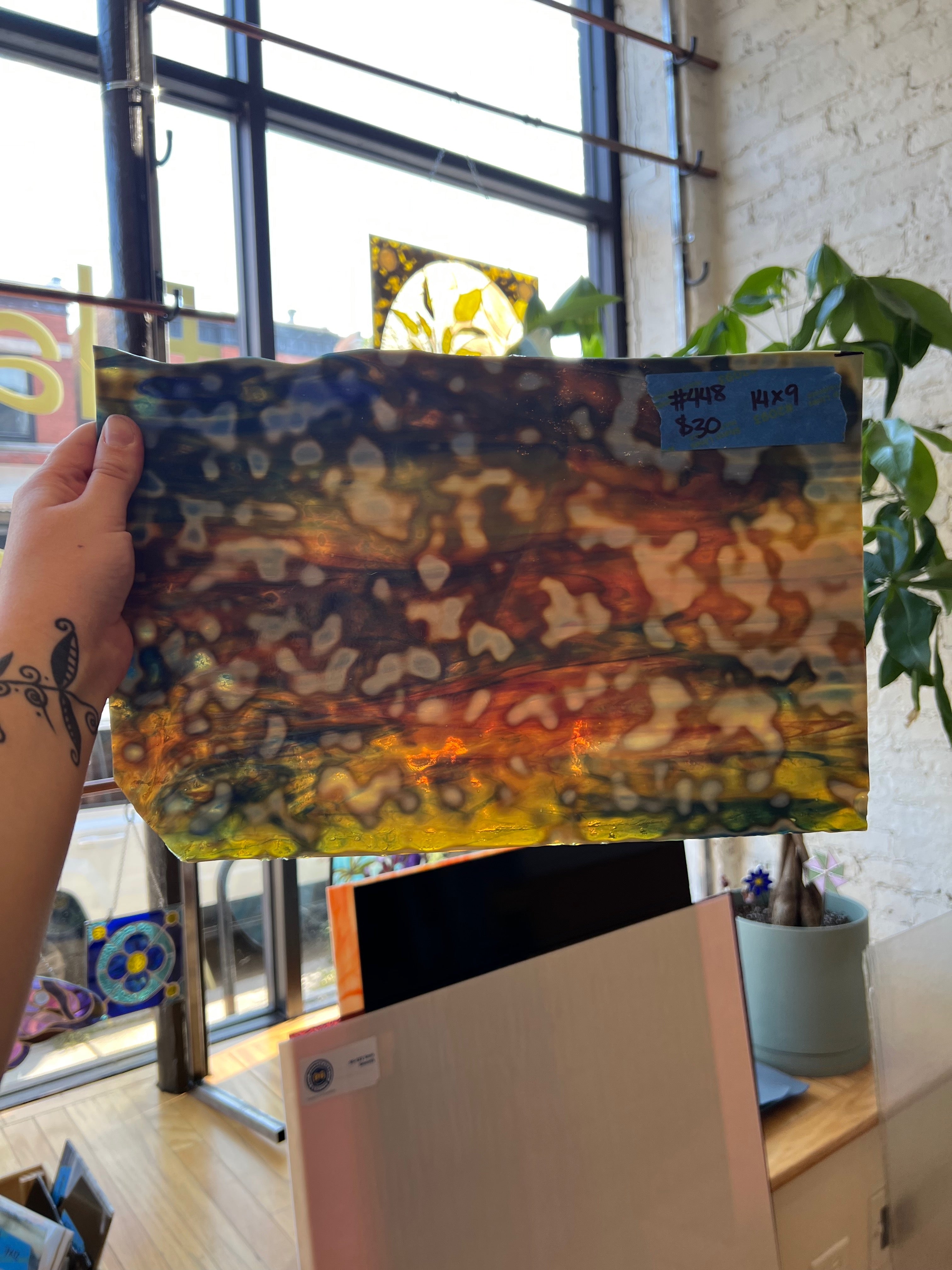 Person holding a colorful glass sheet with abstract patterns in front of a window.