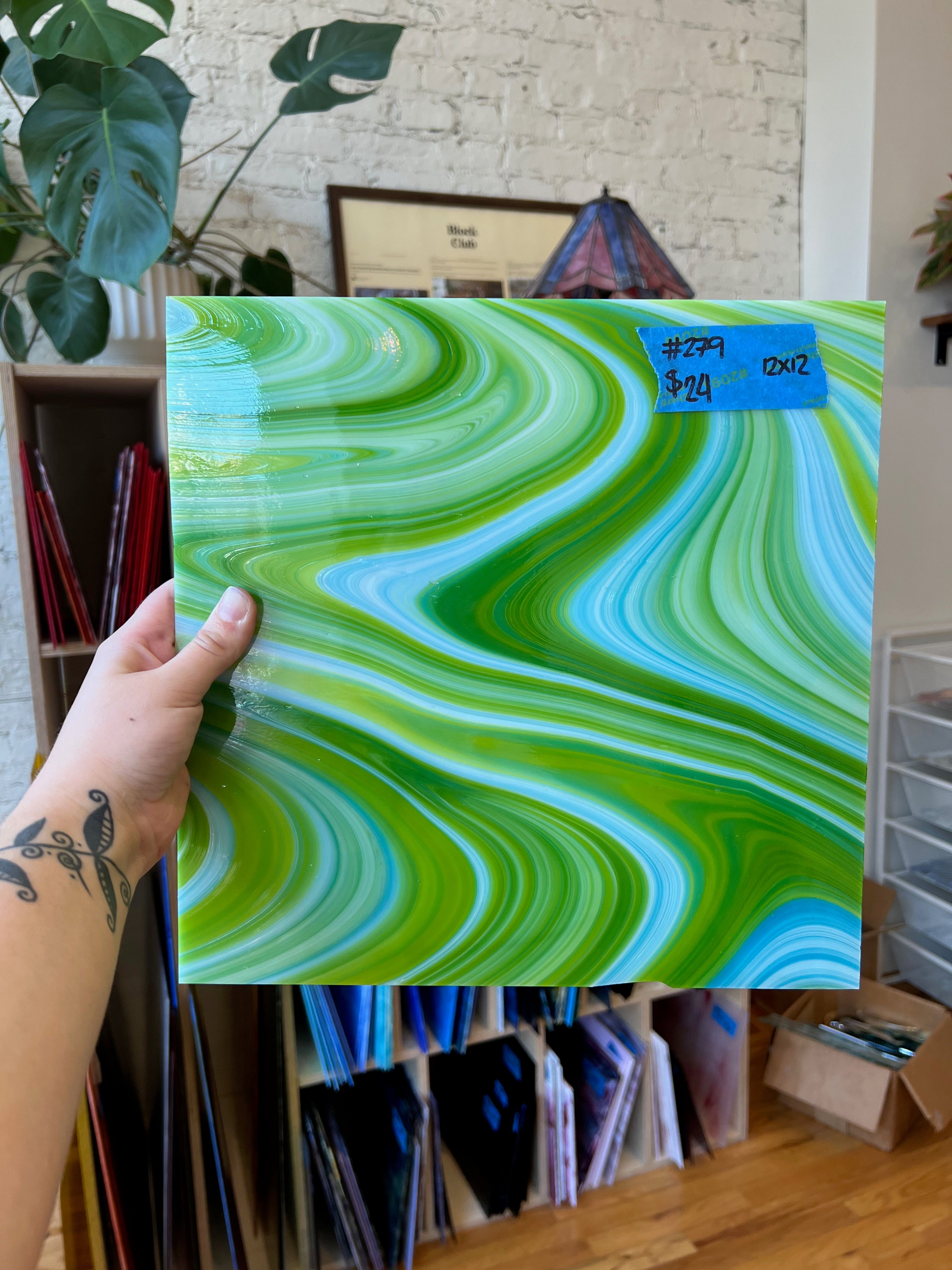 Hand holding a glass sheet with green and blue wavy patterns in an indoor setting.